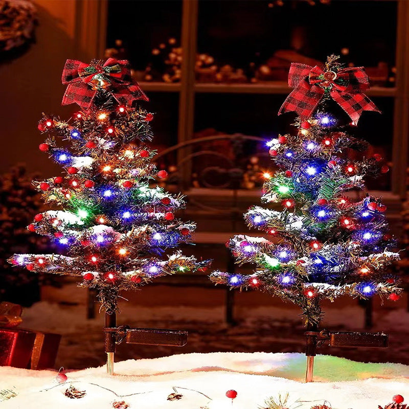 Solar Christmas tree stake light illuminated beside a front door wreath during a snowy Christmas evening