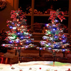 Solar Christmas tree stake light illuminated beside a front door wreath during a snowy Christmas evening