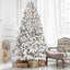 Mixed flocked Christmas tree with warm glowing lights surrounded by holiday decorations