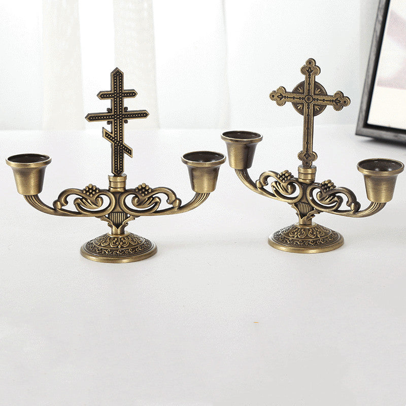 Single cross style candle holder ornament beside a lit candle for ambiance