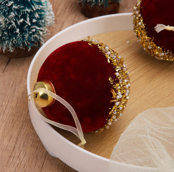 Burgundy flocked glass Christmas ornament hanging on tree branch with warm lighting