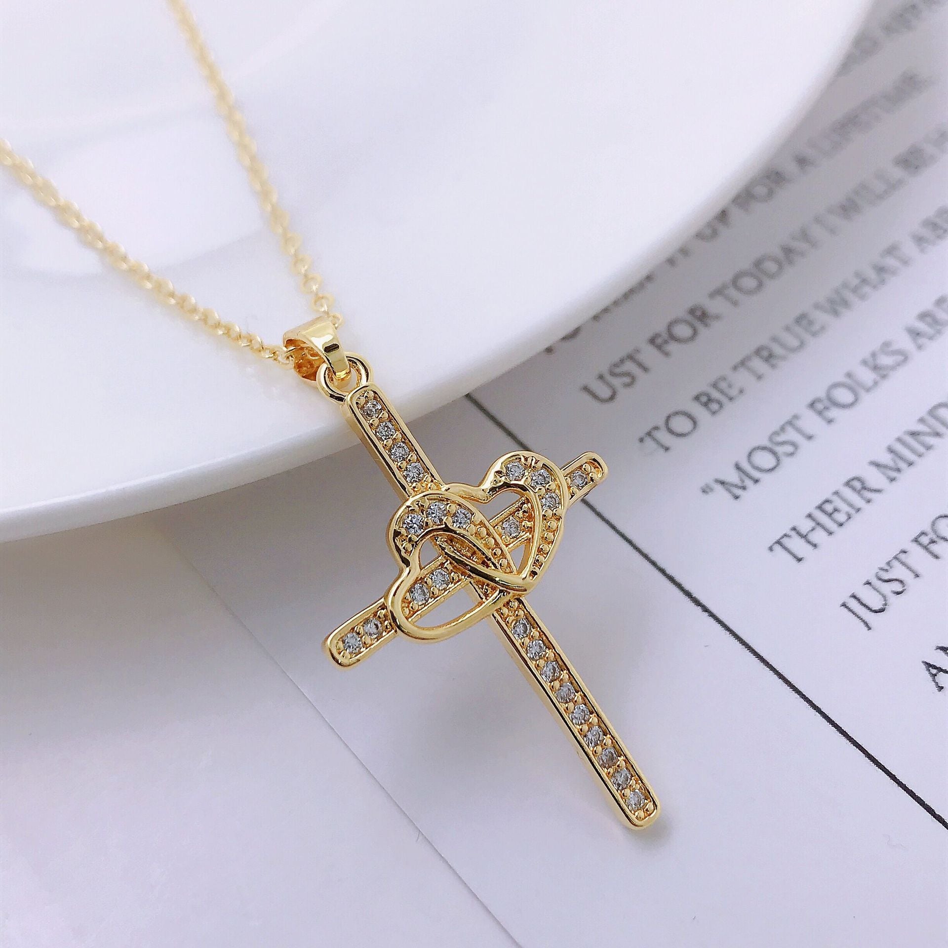 Gold cross necklace laid flat against neutral background