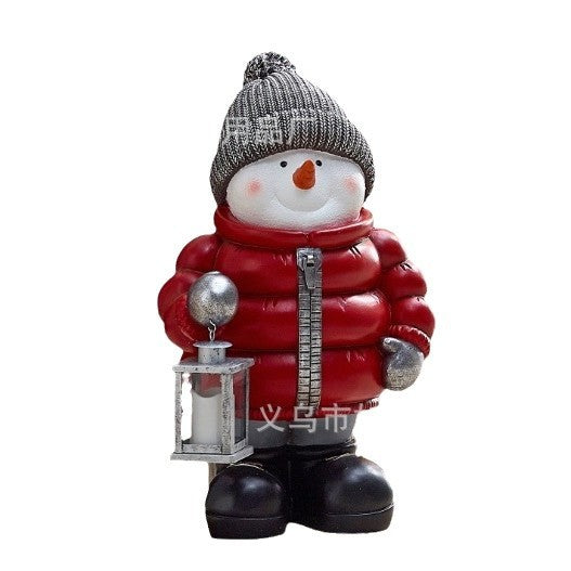 Snowman ornament in red down jacket on snowy Christmas tree with twinkling lights