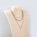 Close-up of geometric cross pendant on layered Cuban chain necklace